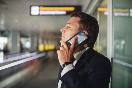 Profile of businessman having conversation on handy. He standing at lobby and seriously looking...