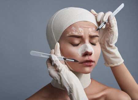 Sad young lady having bandages on the head and lines on the forehead with scalpels near itの写真素材