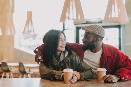 Couple in cafe. Cheerful young lady sitting in the cafe next to her beloved man and enjoying drinking coffee with himの写真素材