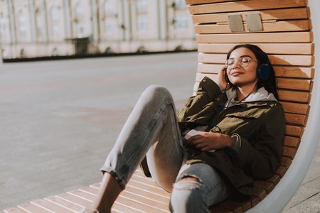 Pleasant young delighted woman lying on the bench while listening to musicの写真素材
