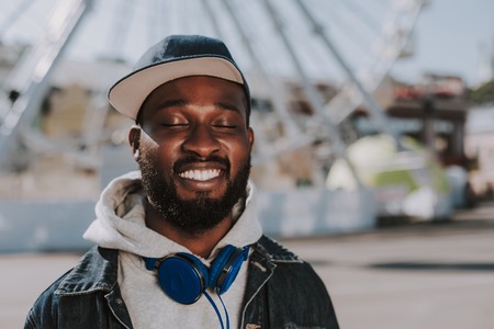 Close up of a pleased young afro American man smiling while standing with closed eyes in the streetの写真素材