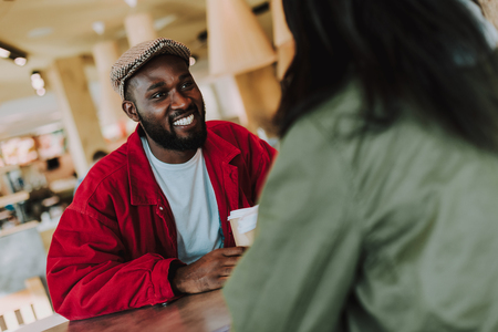 Handsome young man holding cup of coffee and kindly smiling to his beloved woman in a cafeの写真素材