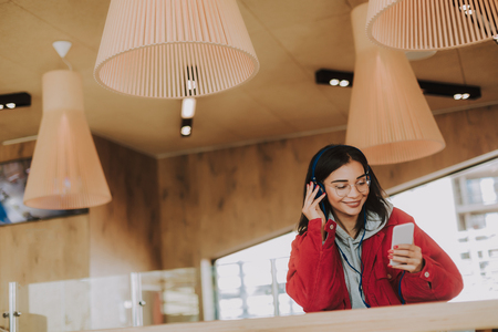 Waist up of a pleasant delighted young woman standing in the cafe while listening to musicの写真素材