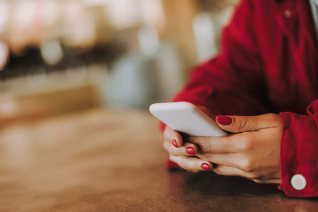 Close up of a modern pone in hands of a woman holding it while sitting at the tableの写真素材