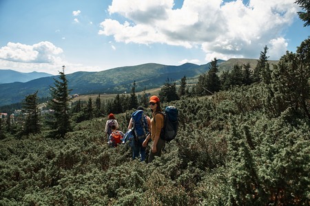 Three women and man walking along path to peak while carrying rucksacks. Grinning lady turning round and looking at cameraの写真素材