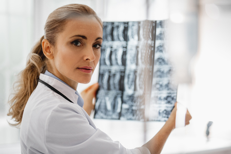 Portrait of beautiful young lady in white lab coat analyzing radiography results.の写真素材