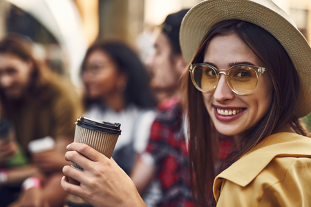 Close up of beautiful young woman wearing lovely stylish hat and smiling while sitting with a cup of coffeeの写真素材