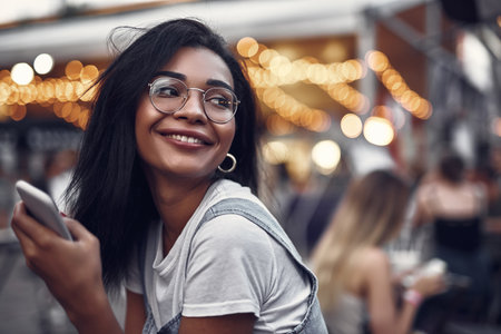 Portrait of hipster young lady in glasses holding smartphone and looking away with smile.の写真素材