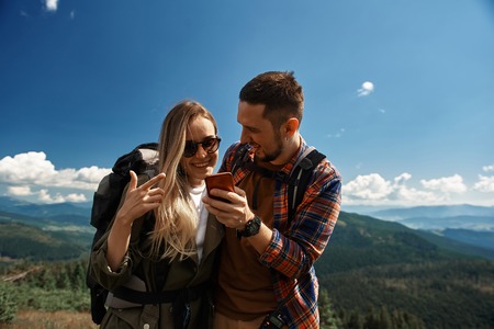 Joyful man showing mobile phone to smiling woman while they are standing on top.