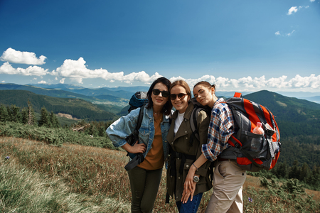 Waist up portrait of three smiling women exploring mountainous landscapes together.の写真素材