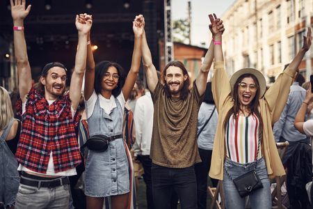 Portrait of young stylish people holding arms and jumping while enjoying outdoor music concert