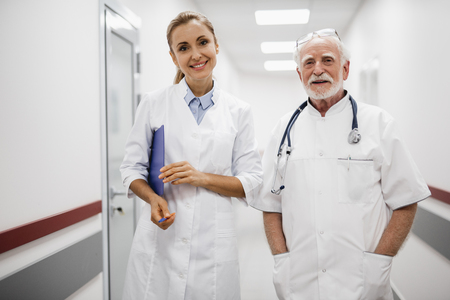 Waist up portrait of beautiful young lady in white lab coat holding clipboardの写真素材