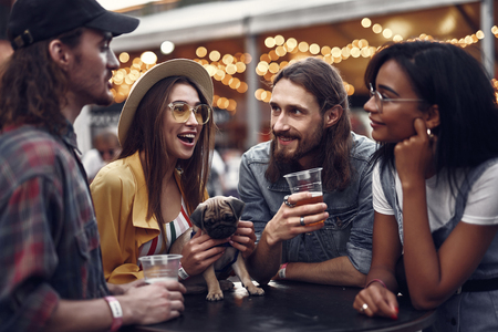 Waist up portrait of stylish hipster friends enjoying drinks while standing at the table.の写真素材