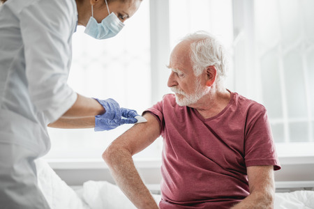 Best treatment for you. Portrait of bearded old man receiving vaccine shot in hand while sitting on hospital bedの写真素材