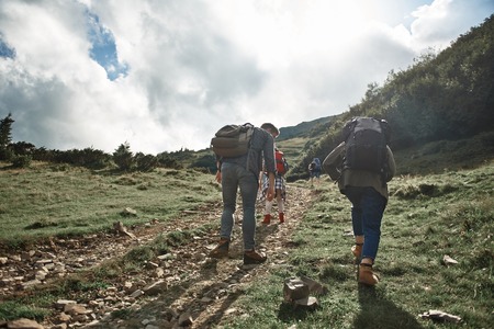 Low angle of four tourists climbing mount together. Three women and one man carrying backpacks while travelling in highland on sunny dayの写真素材