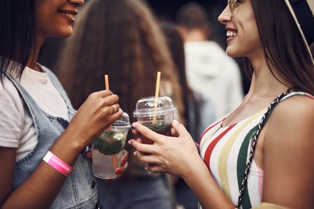 Cropped portrait of young smiling ladies holding drinks with mint. They looking at each other and smilingの写真素材