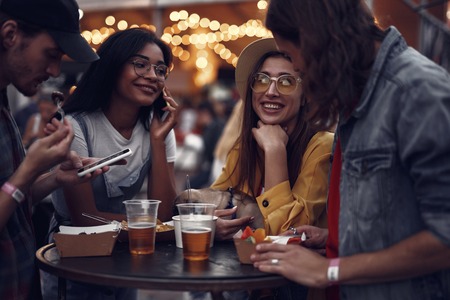 Portrait of young people standing at the table, chatting and using smartphones. Smiling girl in hat holding cute pug dogの写真素材