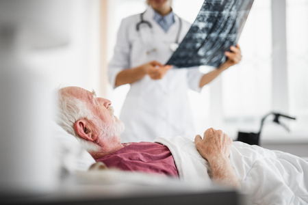 Side view portrait of bearded gentleman resting in hospital room while female physician talking about radiography results. Focus on patientの写真素材
