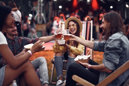 Portrait of handsome bearded guys holding cups with bear and toasting while ladies smilingの写真素材