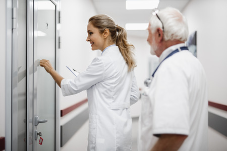 Side view portrait of beautiful young lady in white lab coat holding clipboard and planning to visit patient.の写真素材