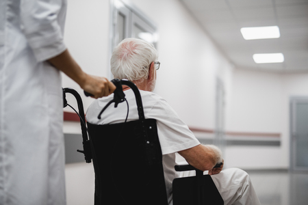 Back view portrait of old gentleman sitting in wheelchair while female medic standing behindの写真素材