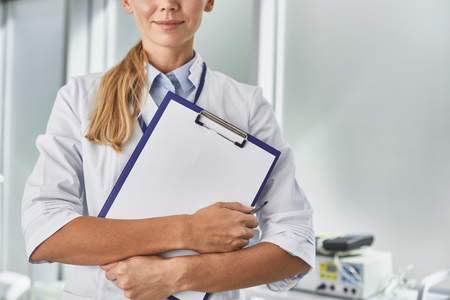 Ready to work. Cropped portrait of smiling woman in white lab coat holding papers and penの写真素材