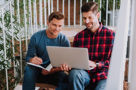 Waist up portrait of young architects are considering working plan of new project while sitting on ladderの写真素材