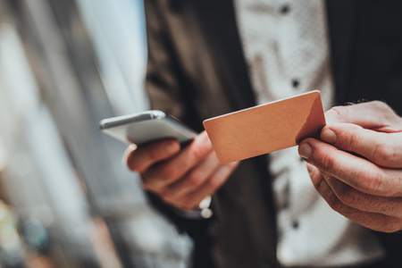 Close up of a credit card in hands of a businessman holding it while using online banking serviceの写真素材