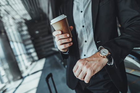 Close up of a coffee cup in hands of a businessman standing at the railway stationの写真素材