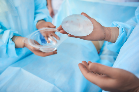 Careful doctor wearing rubber gloves while conducting plastic surgery and holding silicone implantの写真素材