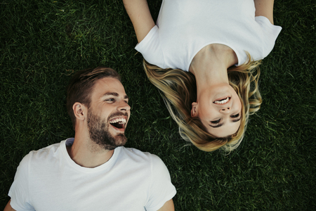 Top view of cheerful young couple is lying on lawn. Woman looking up and man glancing at her while both smilingの写真素材
