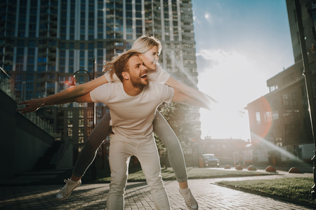 Let fly together. Hilarious active couple are positioning as they were plane. Man holding happy girl on his shoulderの写真素材