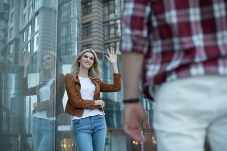 Waist-up portrait of hilarious young woman leaning against glass wall and looking at manの写真素材