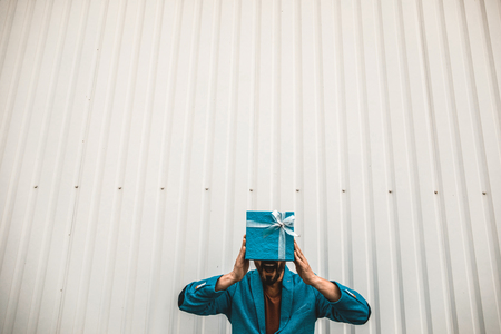 Cheerful expressive young man hiding his face behind the present and opening his mouthの写真素材