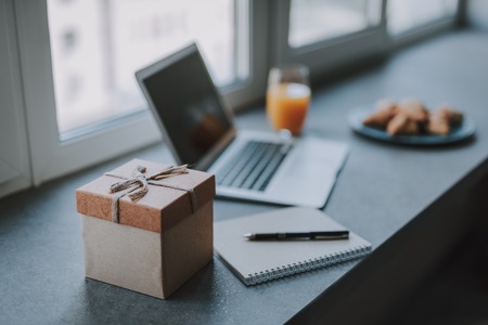 Workplace at home. Gift box in vintage style with blurred laptop, glass of juice and bakery products on backgroundの写真素材