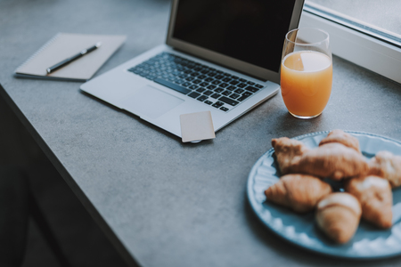 Workplace on the windowsill with laptop, notebook, pencil and continental breakfastの写真素材
