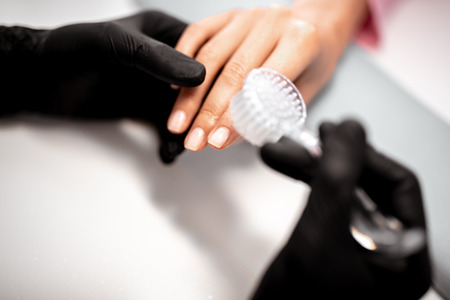 Close up of the professional manicurist in rubber gloves cleaning the nails of his client while using special nail brushの写真素材