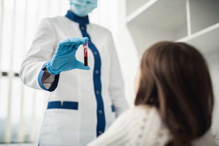 Professional facility investigations in healthcare system. Low angle waist up portrait of female laboratory worker showing test tube with blood to little girlの写真素材