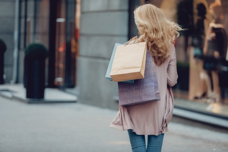 I am heading to the store. Back view portrait of middle-aged woman carrying colorful shopping bagsの写真素材
