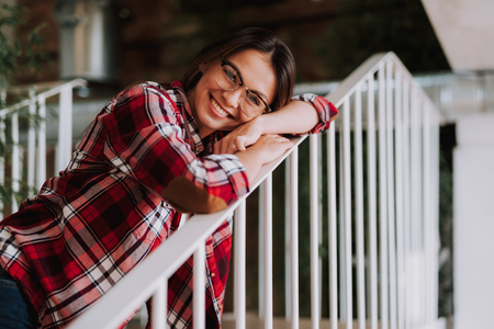 Portrait of charming woman in plaid shirt putting head on hand while looking at camera and smilingの写真素材