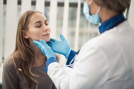 Concept of professional consultation in therapist system. Close up portrait of doctor woman examining tonsils of smiling young lady in medical officeの写真素材