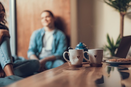 Calm people relaxing near the window while their cups of tea with lovely hearts standing on the...