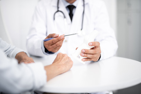 Professional general practitioner sitting at the table with his patient and holding a pen while...