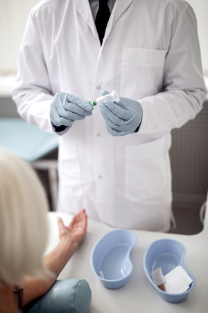 Experienced doctor in white uniform standing in front of his patient and holding vacuum blood collection needleの写真素材