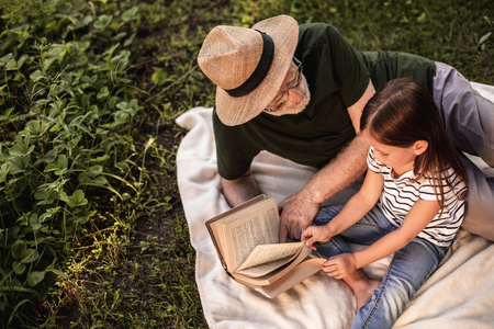Top view of little girl with her grandparent spending time in fresh air and reading storiesの写真素材
