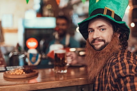 Close up portrait of smiling gentleman in green leprechaun hat sitting at bar counter. Copy space in left sideの写真素材