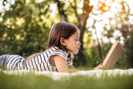 Low angle picture of pretty girl kid lying on green grass and looking at open bookの写真素材