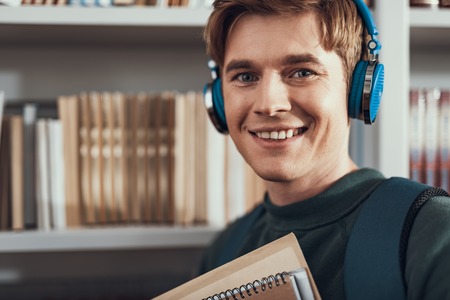 Enjoying music. Portrait of the positive young man smiling and looking happy while listening to...