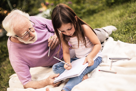 Grandad with cute female child doing school homework in yardの写真素材