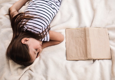 Top view of sleeping kid lying on bed next to unfinished bookの写真素材